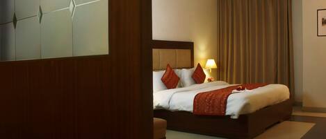 Una habitación de hotel con una cama grande, cabecera, mesita de noche, lámpara y ventilador de techo.
