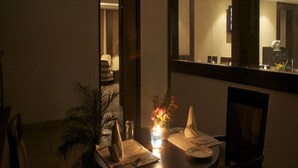 A dimly lit dining area with a table set for two, a potted plant, and a vase with flowers. - Legend Sarovar Portico Baddi (Baddi)