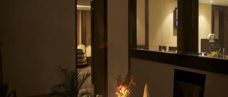 A dimly lit dining area with a table set for two, a potted plant, and a vase with flowers.