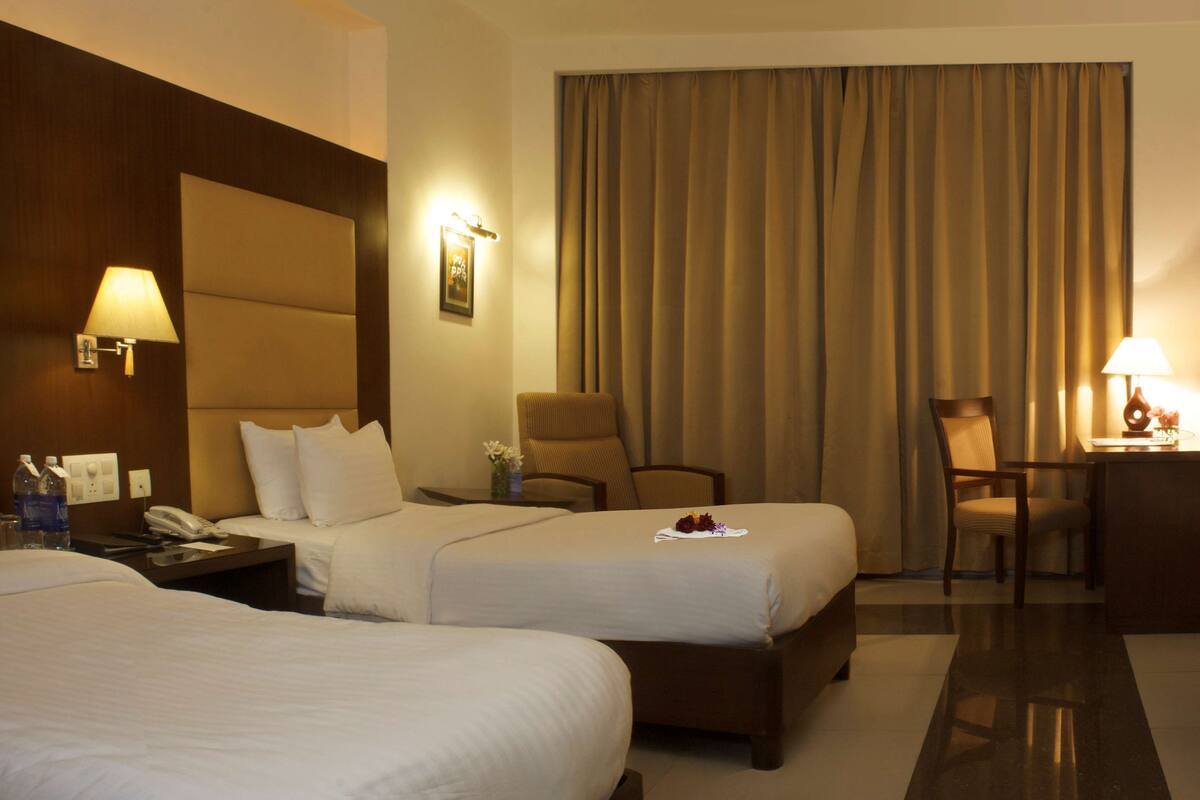 Ein Hotelzimmer mit zwei Betten, einem Schreibtisch, einem Stuhl und einem großen Fenster mit Vorhängen.