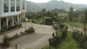 A modern building with large windows, a landscaped courtyard, and a view of distant hills. - Legend Sarovar Portico Baddi (Baddi)