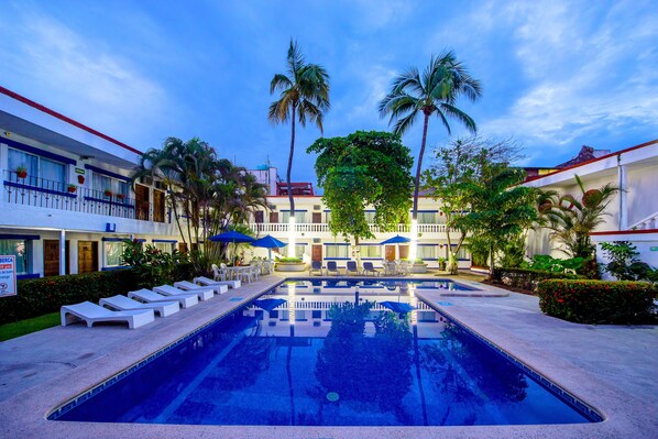 Ein Hotel mit Swimmingpool, Liegestühlen und Palmen.