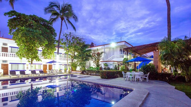 A swimming pool with lounge chairs and umbrellas, surrounded by palm trees and a building with multiple balconies. - Hotel Hacienda Vallarta Playa Las Glorias (Puerto Vallarta)