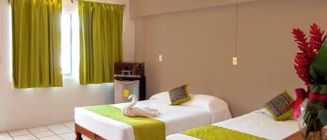 A hotel room with two single beds, a small desk, an air conditioner, and a window with green curtains.
