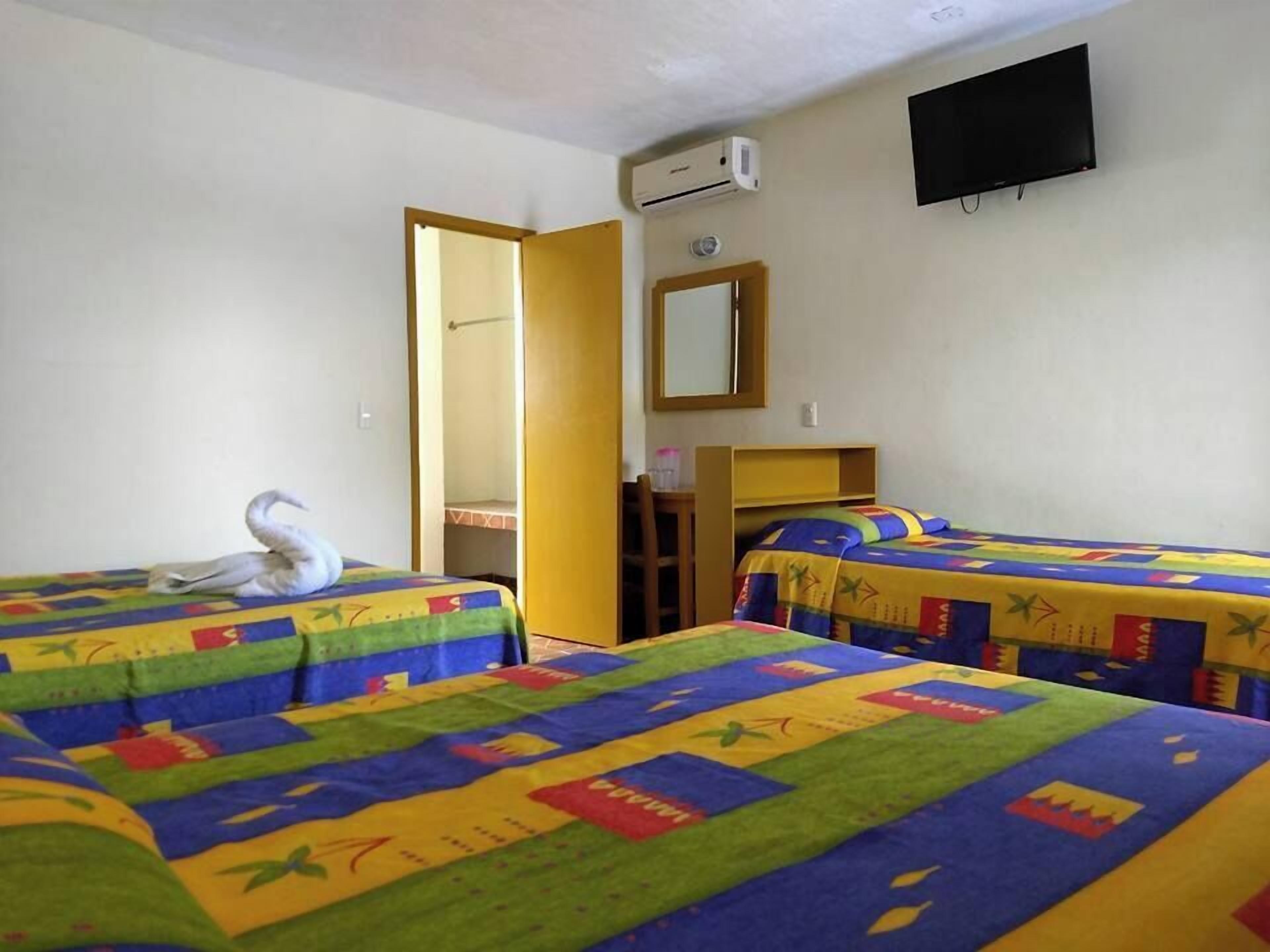 A hotel room with two beds, each with colorful bedding, a television on the wall, and an air conditioning unit.