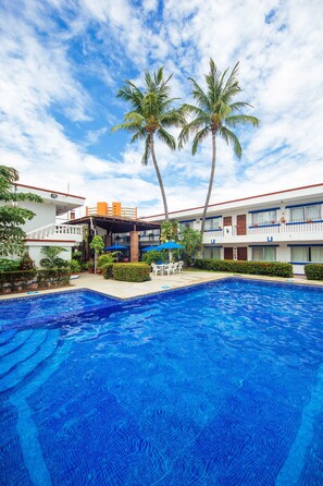 Ein Hotel mit Schwimmbad, Palmen und einer überdachten Terrasse.