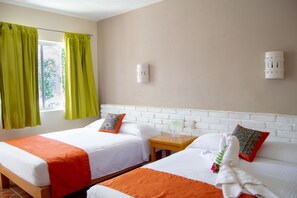 Ein Hotelzimmer mit zwei Betten, einem Fenster mit grünen Vorhängen, einer weißen Ziegelwand und einem kleinen Nachttisch.