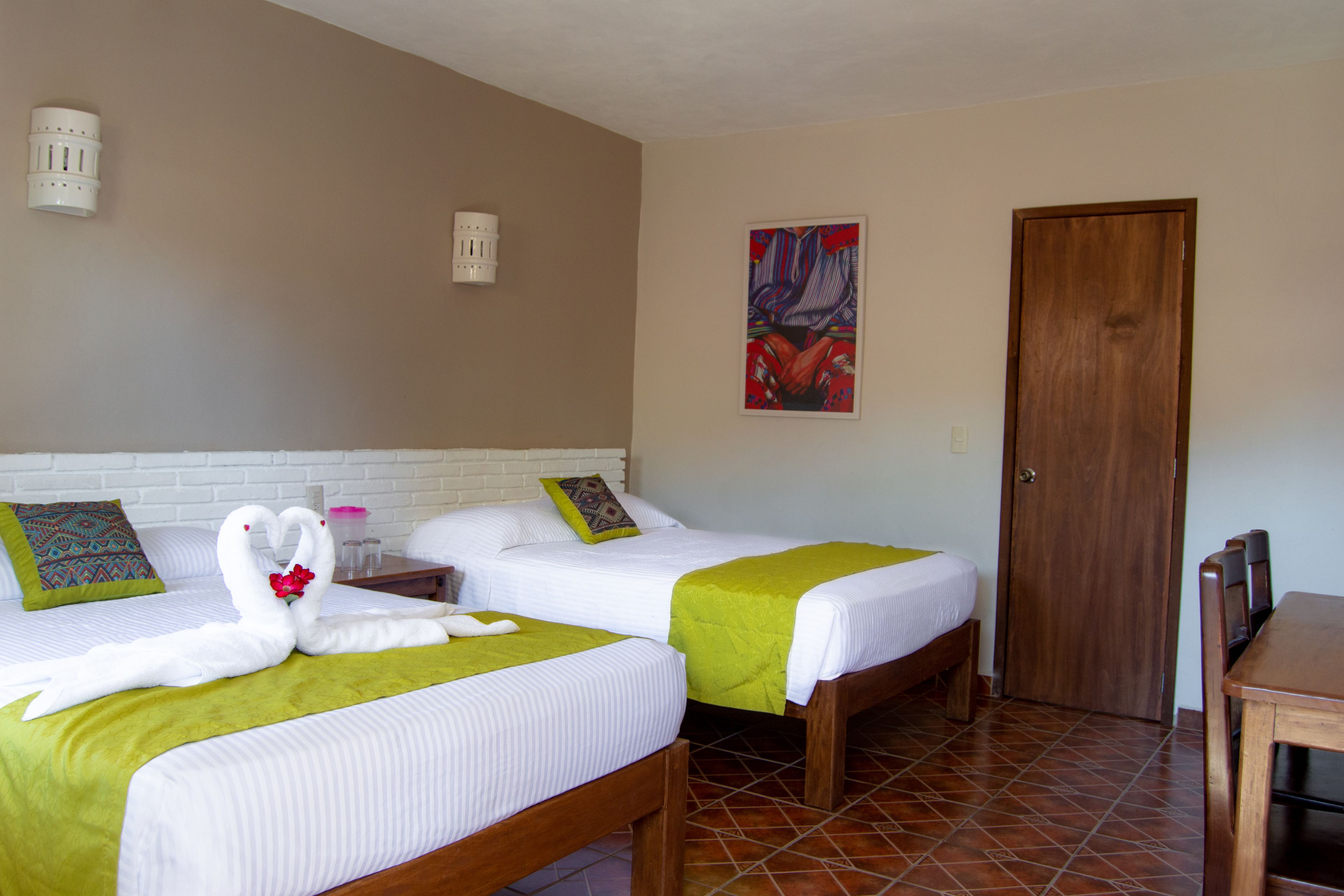 Een hotelkamer met twee bedden, een houten tafel, een deur en een schilderij aan de muur.