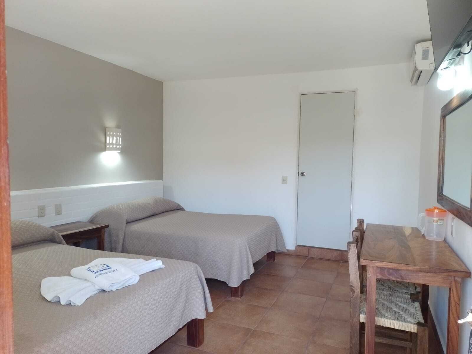 A small, clean room with two beds, a desk, and a mirror.