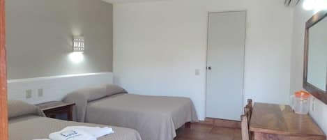A small, clean room with two beds, a desk, and a mirror.