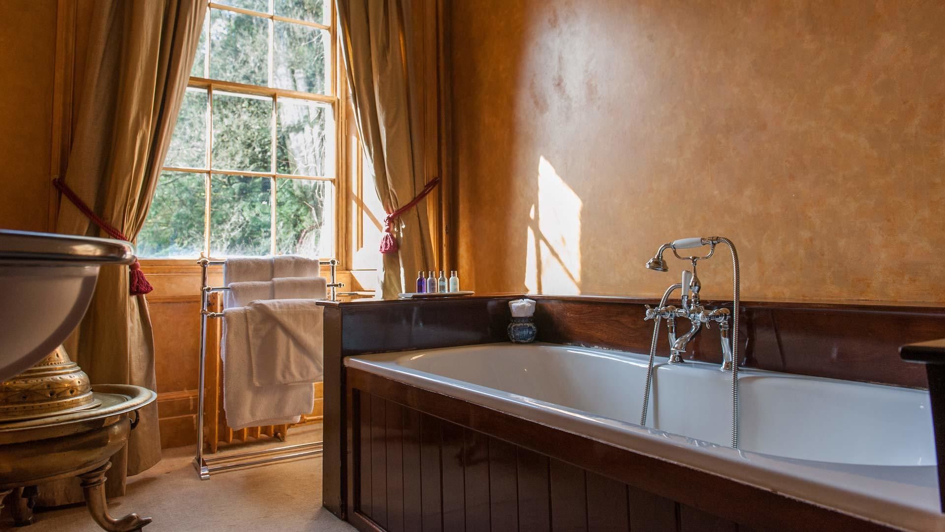 A bathroom with a large bathtub, wooden paneling, a window with curtains, and a towel rack.