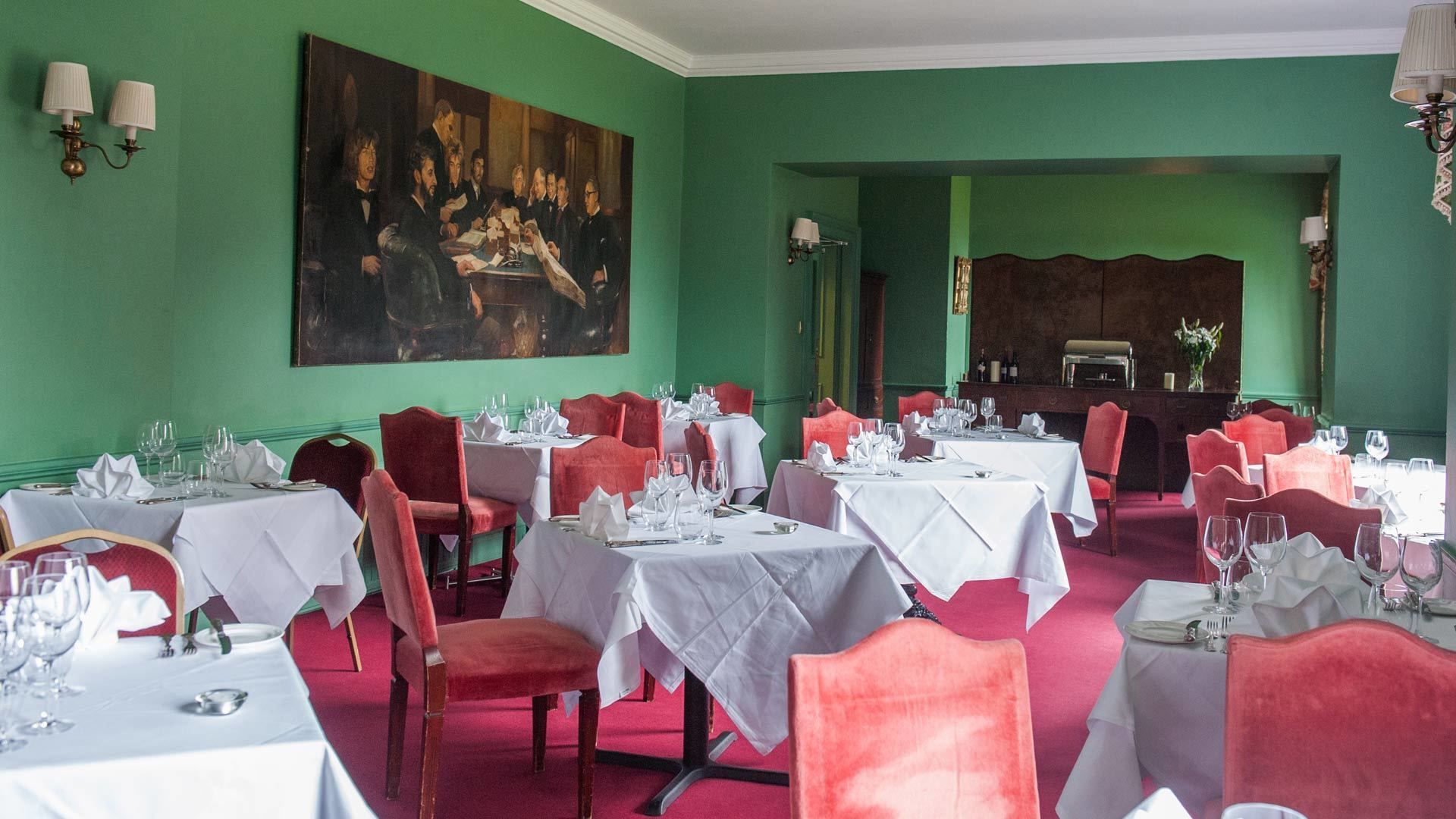 Un comedor con mesas dispuestas para el servicio, un cuadro grande en la pared y una zona de bar al fondo.