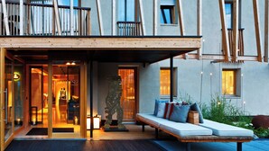 A modern hotel entrance with a glass door, a wooden bench with cushions, and a statue in the courtyard. - Art & Design Hotel Napura (Terlano)