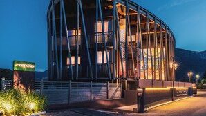 A modern building with a curved glass facade, a prominent entrance with a sign, and a well-lit exterior. - Art & Design Hotel Napura (Terlano)