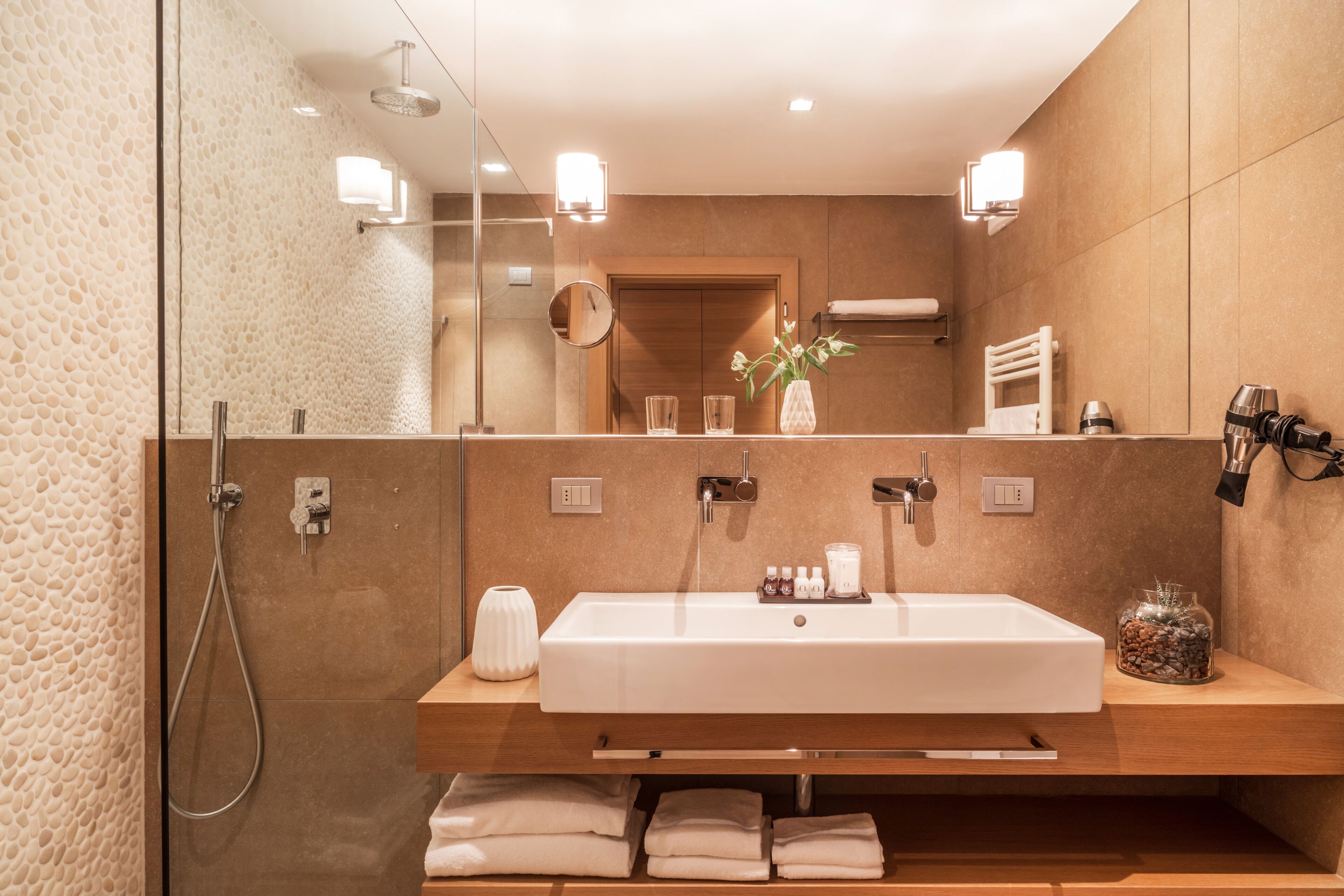 A modern bathroom with a large mirror, a white sink, and a shower.