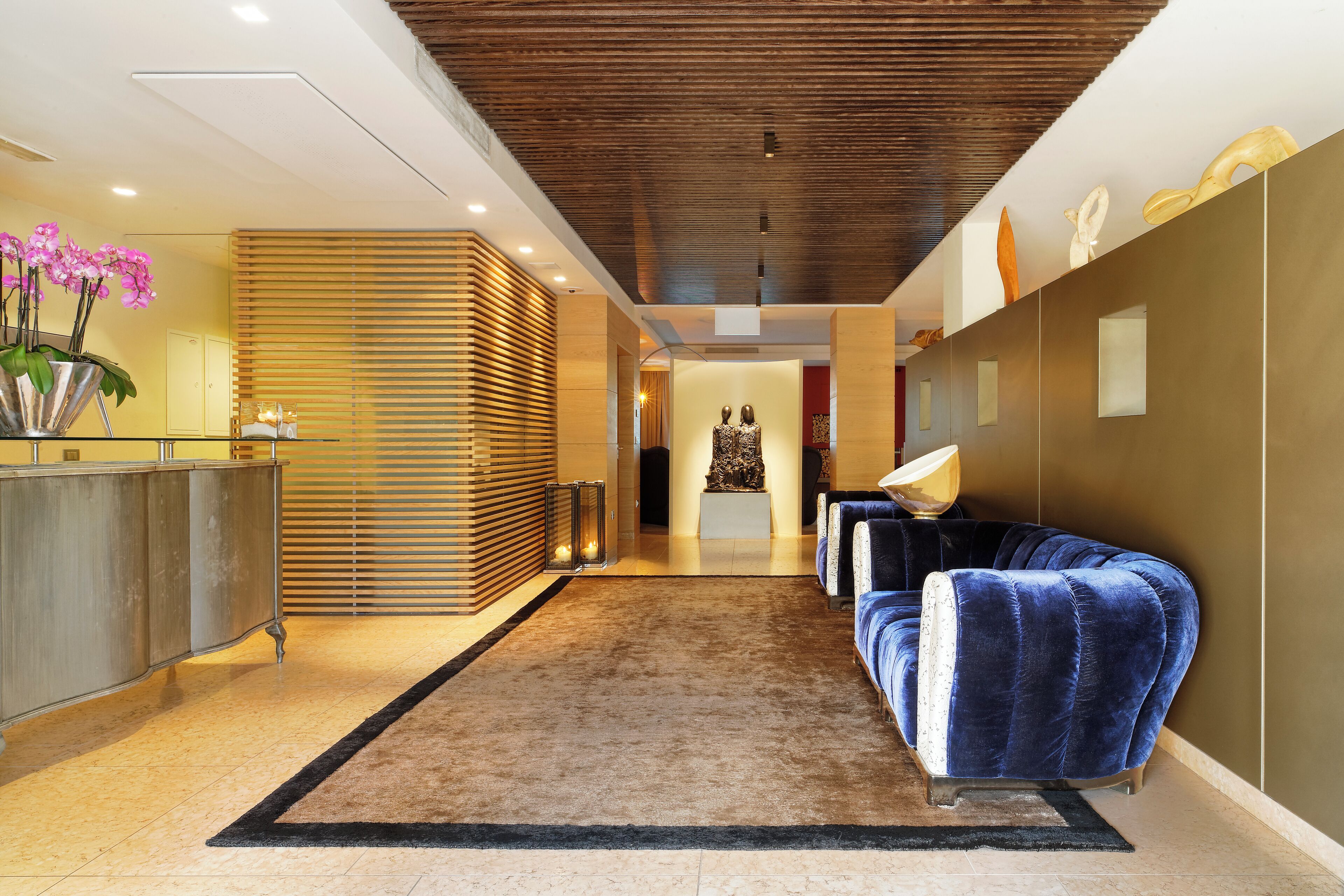 Een moderne lobby met een receptiebalie, een blauwe bank en een decoratieve sculptuur.