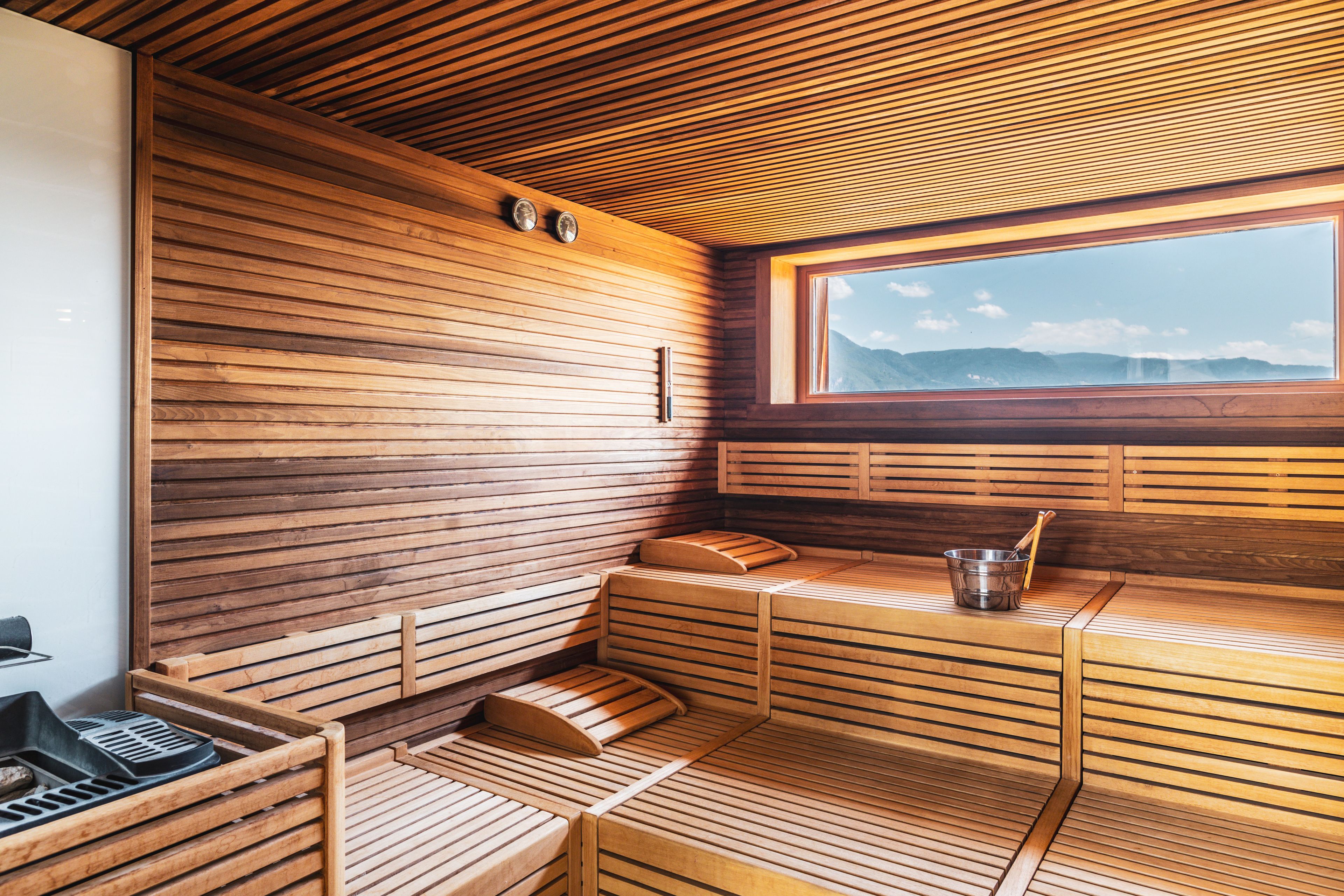 A wooden sauna with benches, a window, and a metal bucket.
