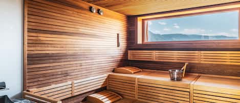 Una sauna de madera con bancos, una ventana y un balde de metal.