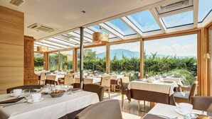 A restaurant with tables set for dining, large windows, and a view of greenery and mountains. - Art & Design Hotel Napura (Terlano)