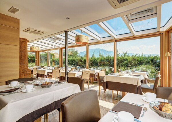 Un restaurante con mesas dispuestas para comer, grandes ventanales y vistas a zonas verdes y montañas.