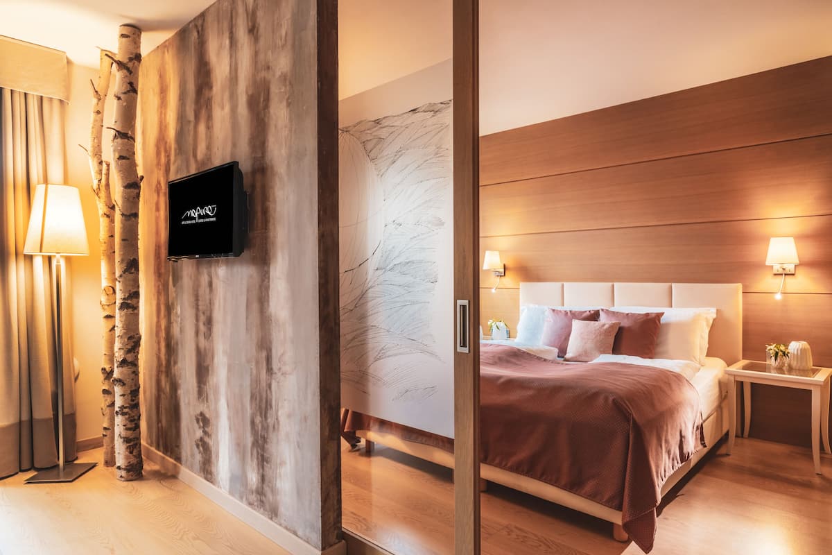 A modern hotel room with a bed, bedside lamps, a TV, and a wooden wall with a marble-like design.