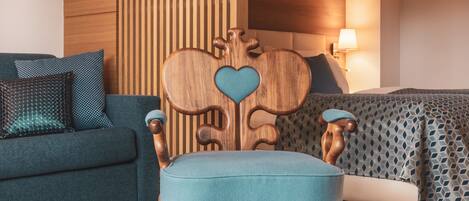 A room with a wooden headboard with a heart-shaped design, a blue upholstered chair, a blue sofa with patterned cushions, and a bed with a geometric patterned bedspread.