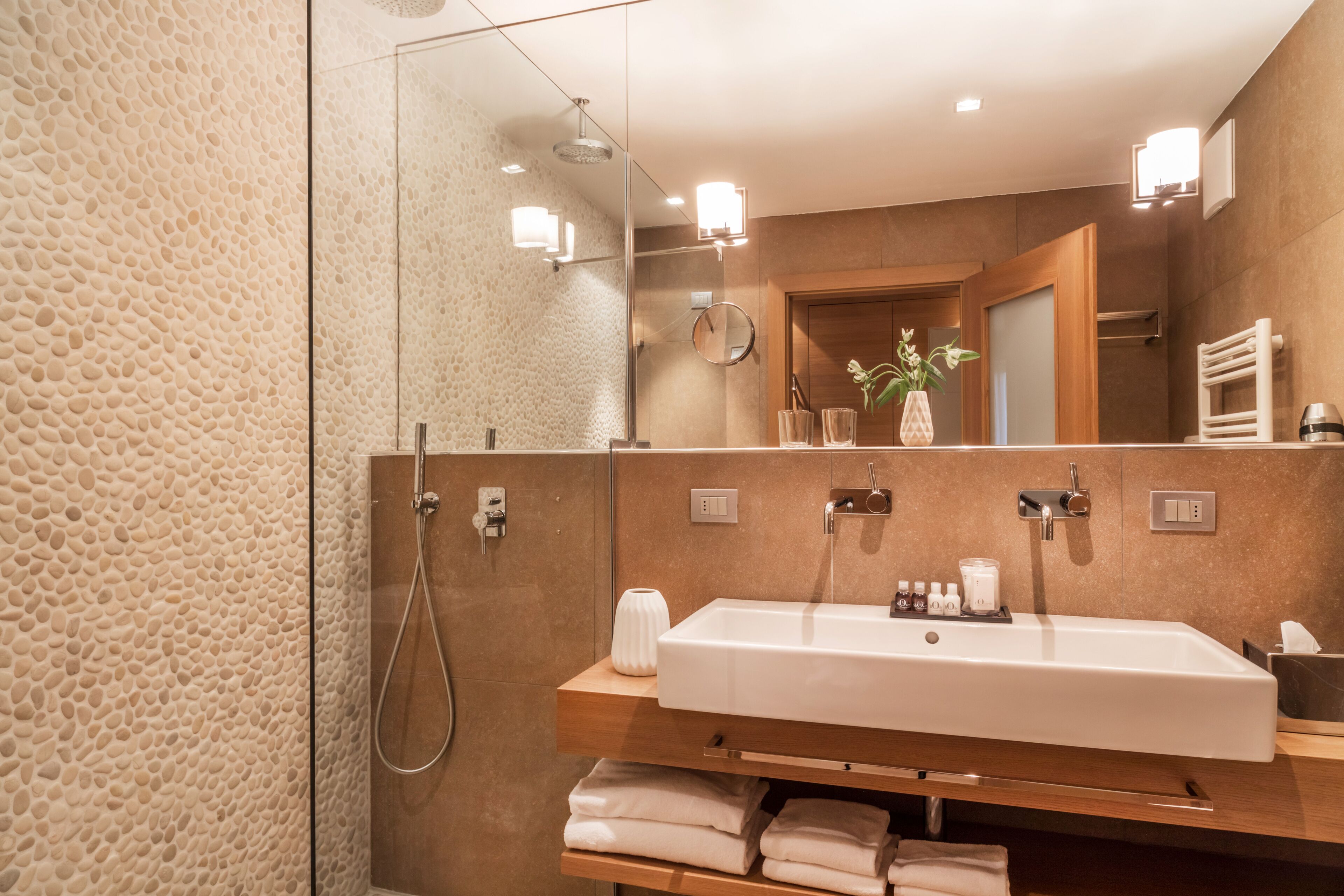 A modern bathroom with a large mirror, a white sink, and a shower.