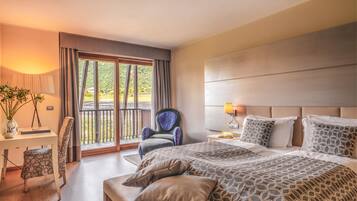 Habitación de hotel con una cama grande, una silla, un escritorio y un balcón con vistas al verdor.