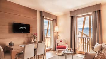 Una habitación de hotel moderna con una pared de madera, un televisor de pantalla plana, una zona de comedor con mesa y sillas, un sillón rojo con diseño de corazón, un sofá y ventanas amplias con vistas a montañas.