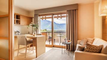 Una habitación de hotel moderna con espacio para cocinar, una mesa de comedor, un sofá y un balcón con vistas a la montaña.