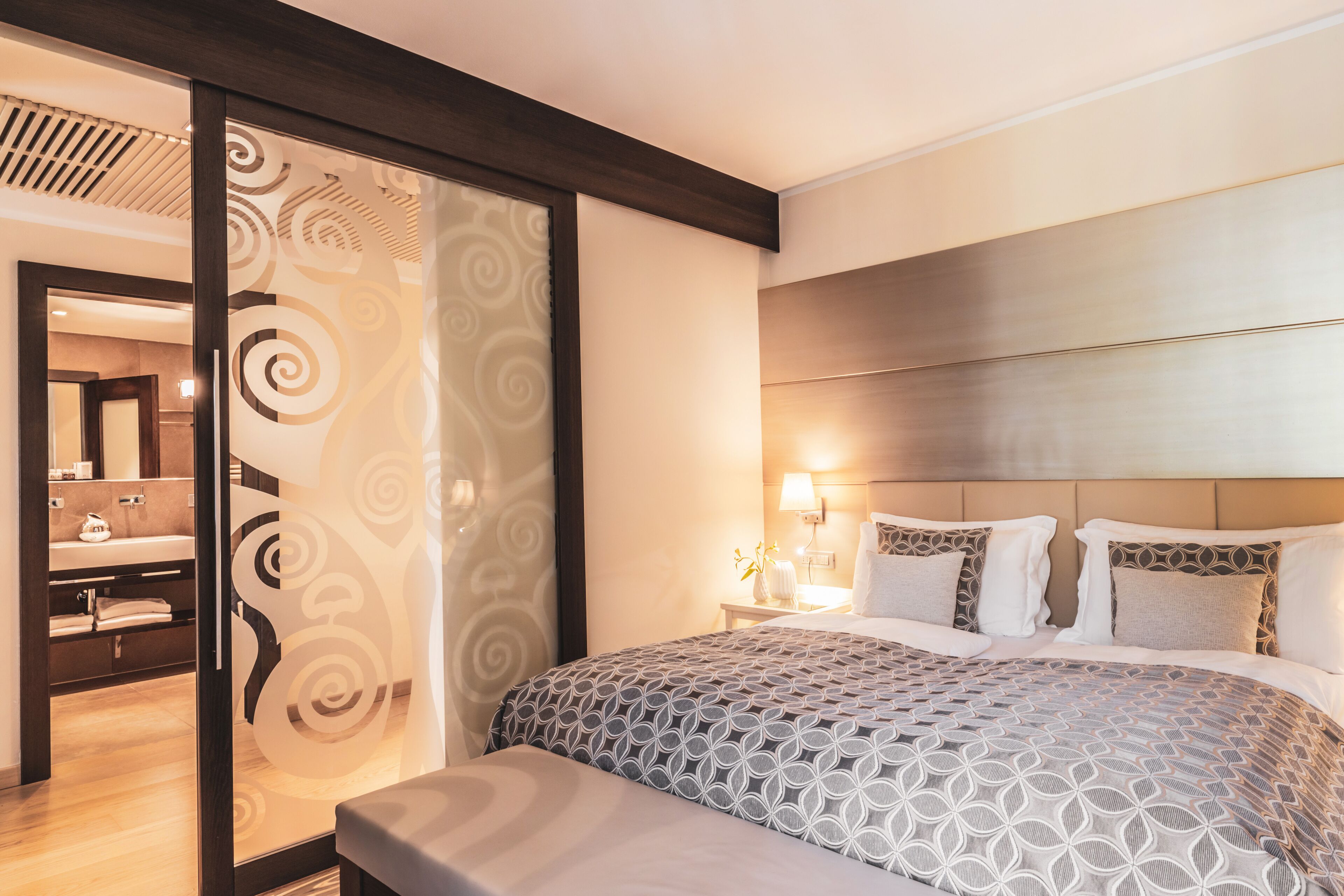Ein modernes Hotelzimmer mit einem großen Bett, einem Nachttisch mit Lampe und Blick ins Bad.