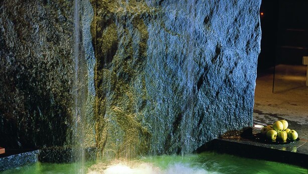 Una fuente de agua con pared de roca y una piscina.