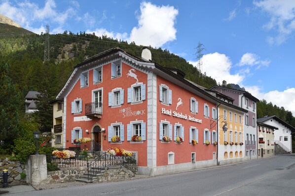 Ein mehrstöckiges Hotel mit roter Fassade, weißen Fensterläden und Blumenkästen an den Fenstersims.