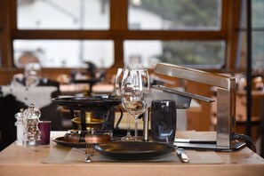 Ein Esstisch, gedeckt mit einem Weinglas, einem schwarzen Teller, einer Gabel, einem Messer, einem Salz- und Pfefferstreuer, einer kleinen violetten Tasse und einem Kerzenhalter.