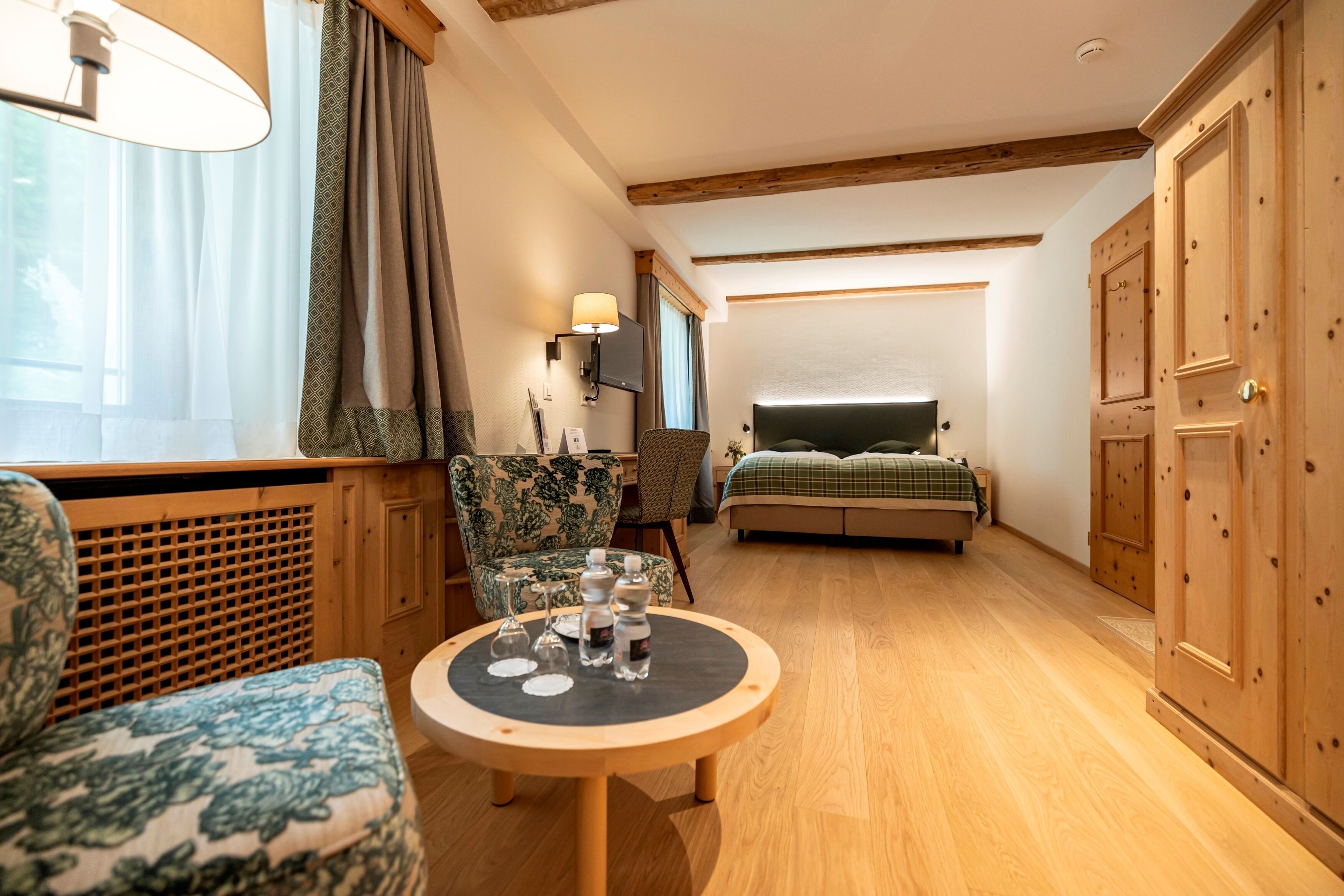 Una habitación acogedora con cama, una silla, una mesa con vasos y botellas, una lámpara y muebles de madera.