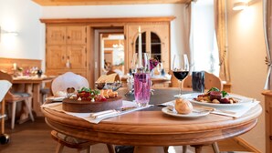 Una mesa de madera con un pastel, platos de comida y copas de vino en una habitación cálidamente iluminada con techos y armarios de madera.