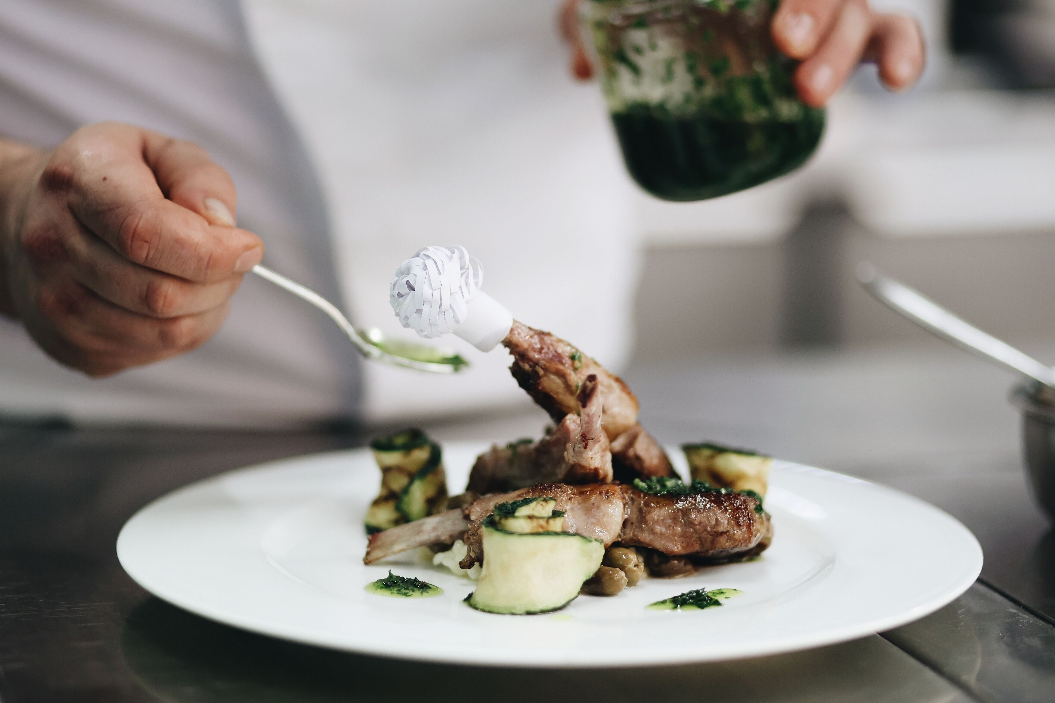 A person serving a dish with meat and vegetables on a white plate.
