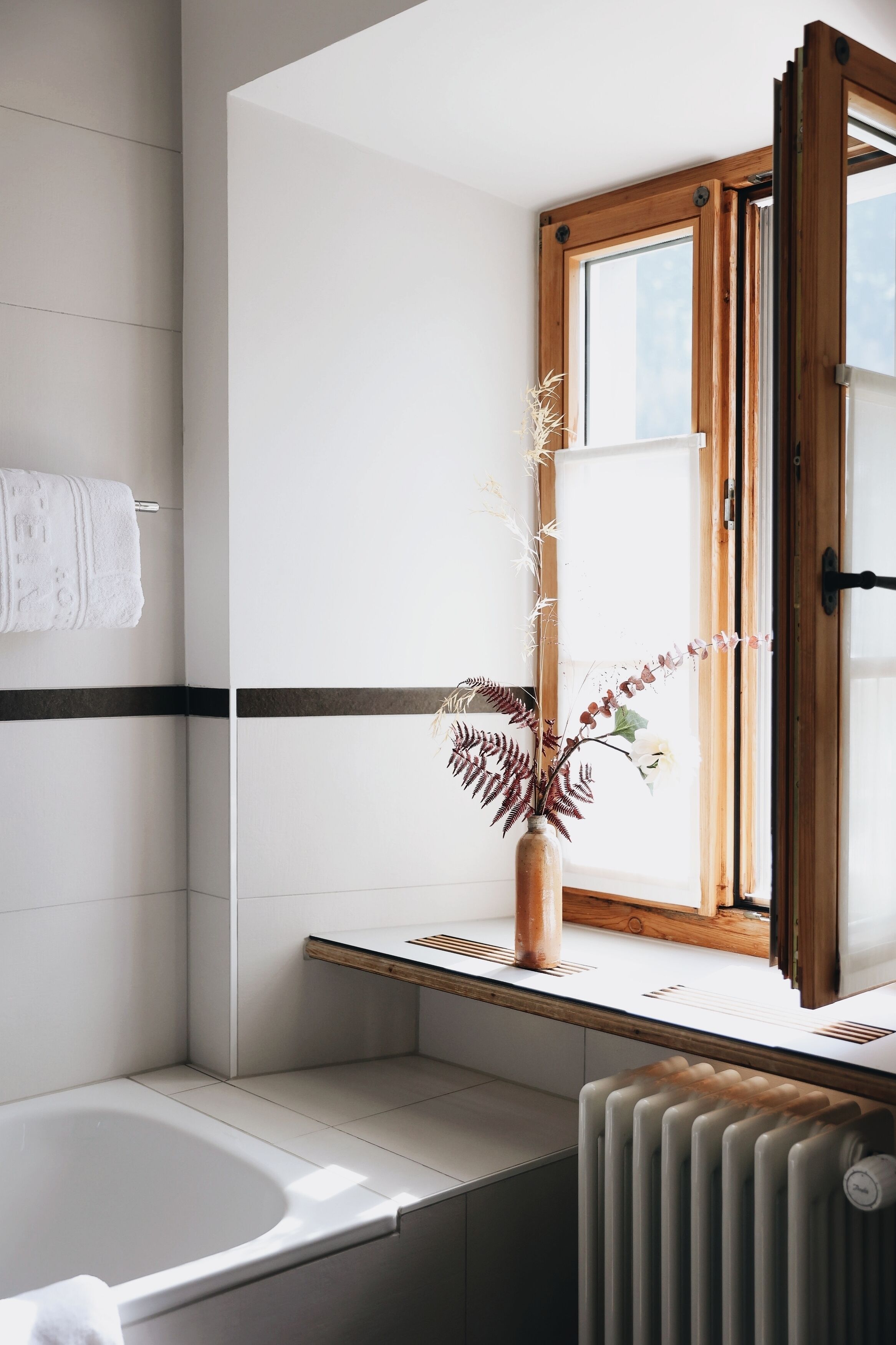 A modern bathroom with a bathtub, a window with a wooden frame, and a radiator.