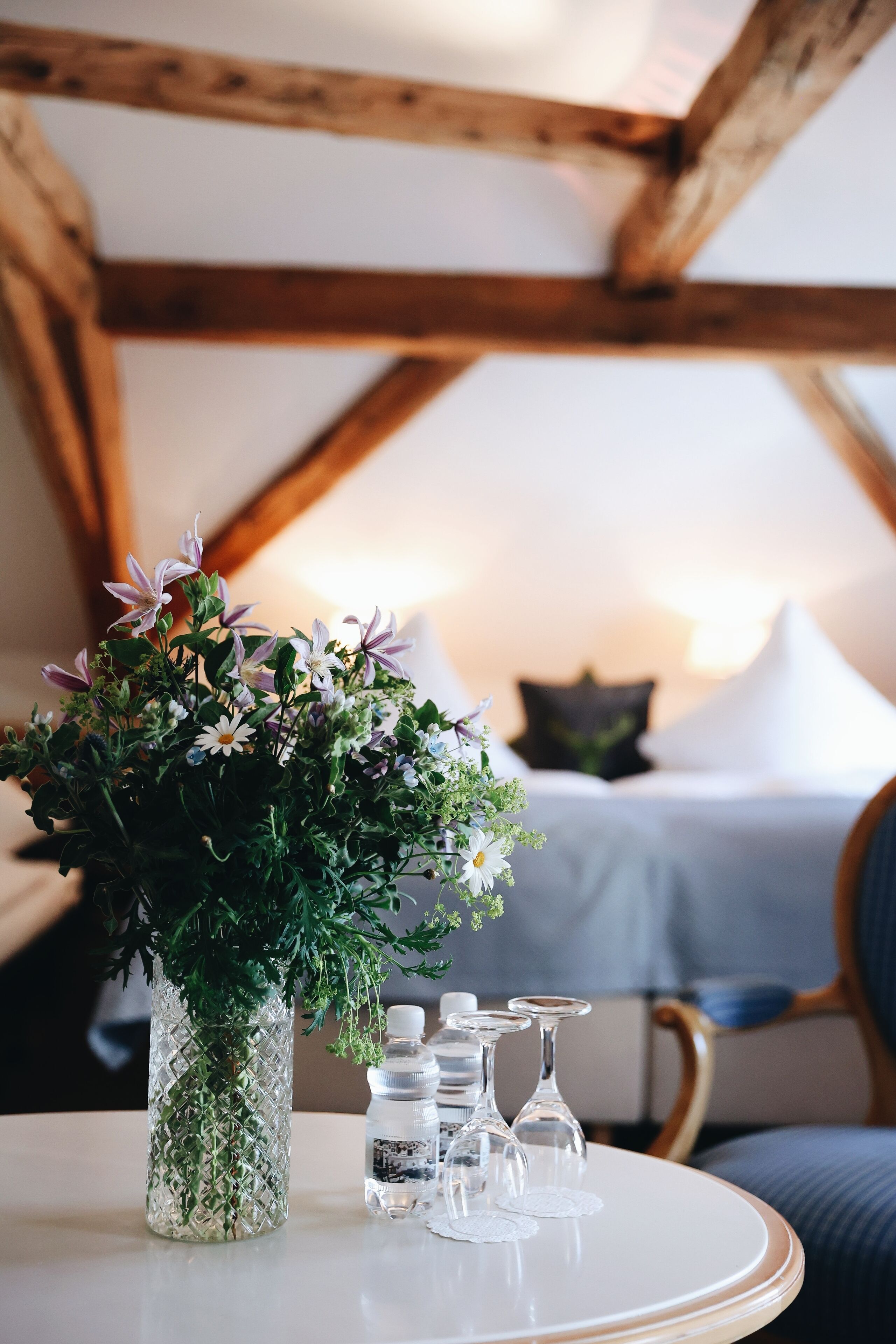 Una habitación con una cama, un jarrón con flores y una mesa con vasos y botellas.