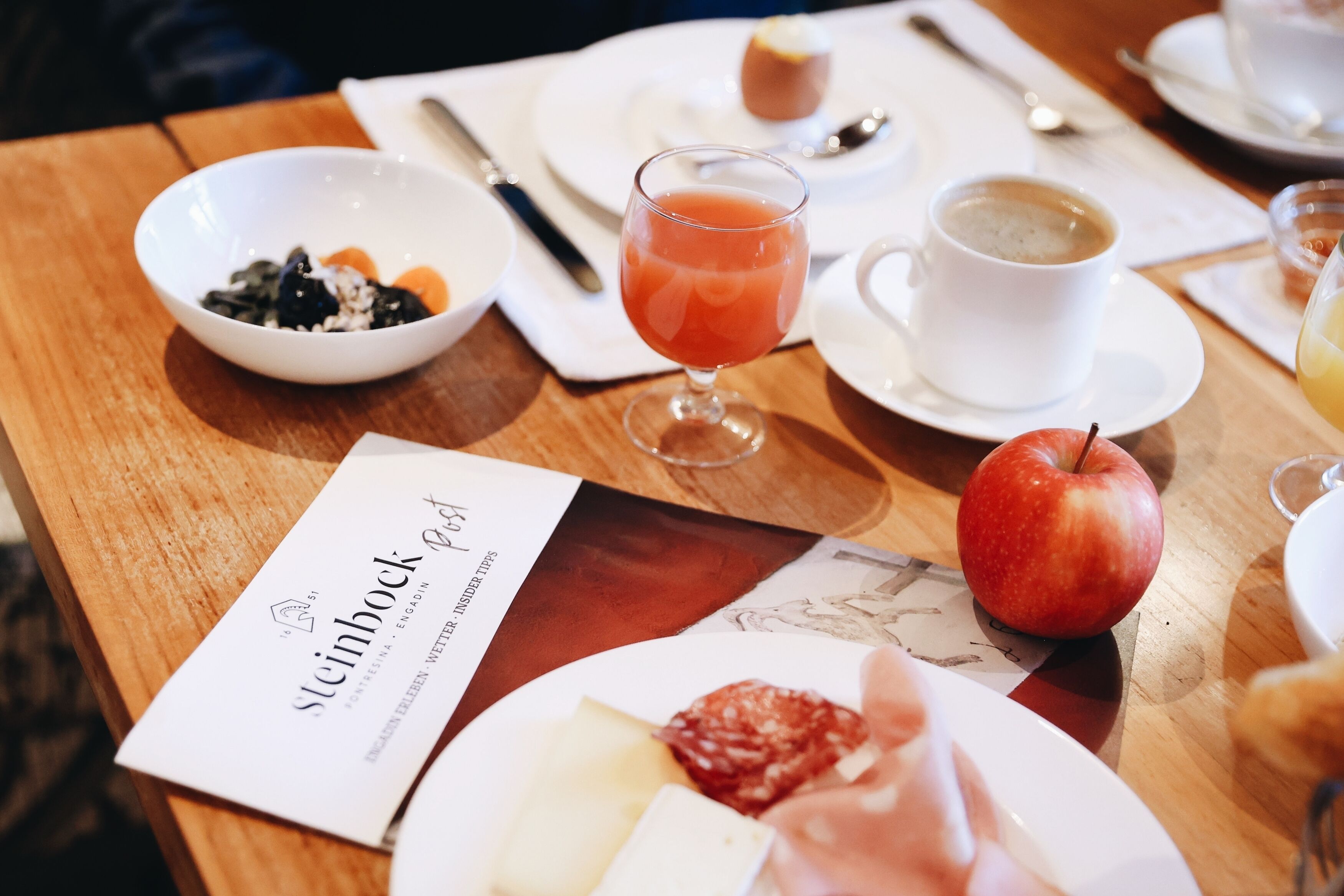 A breakfast setting with a plate of food, a glass of juice, and a cup of coffee on a wooden table.