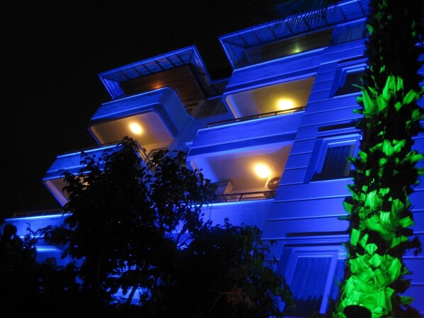 A multi-story building with balconies and a green illuminated structure in the foreground.