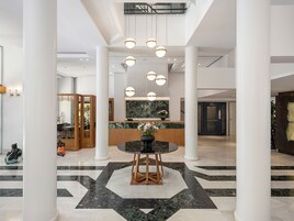 Un vestíbulo amplio con una recepción, una mesa redonda con sillas y un suelo con diseño geométrico.