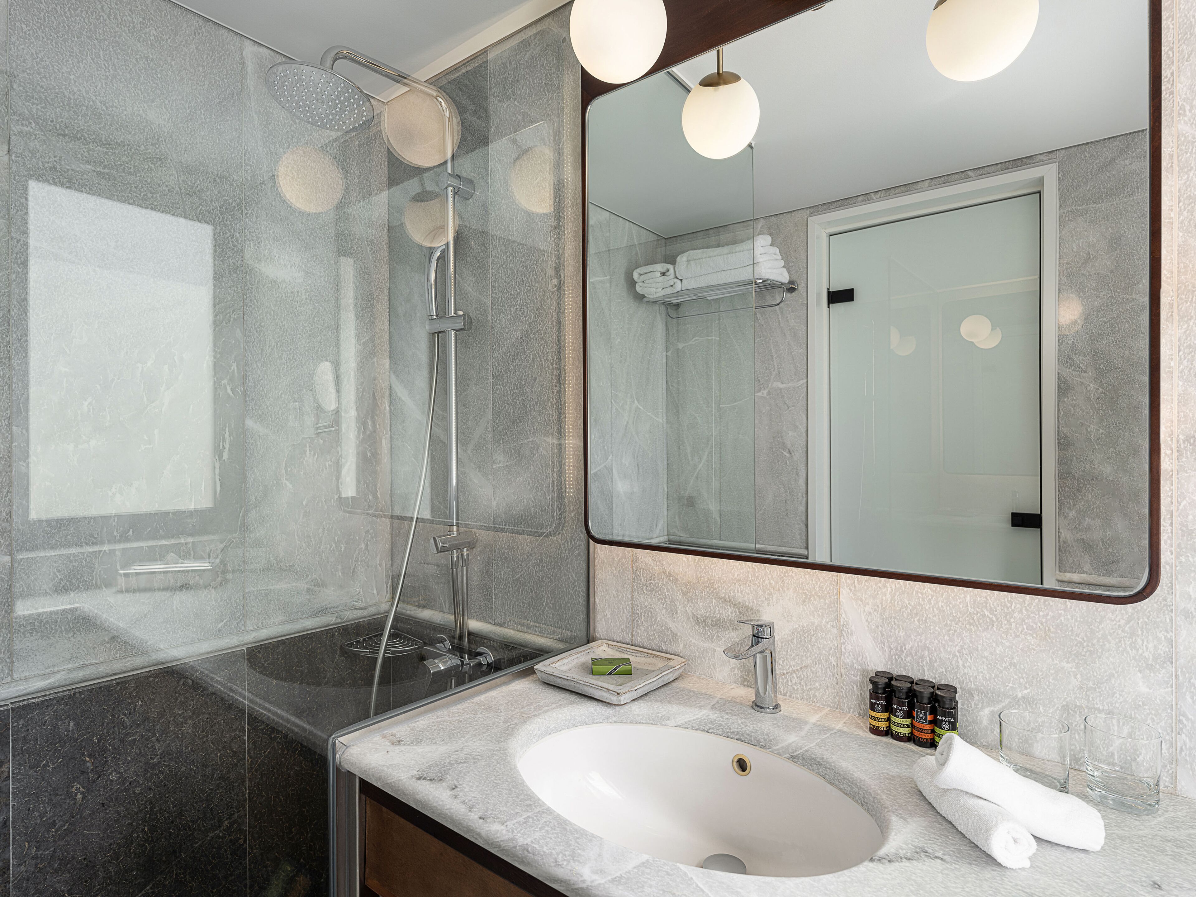 Un baño moderno con ducha acristalada, lavamanos blanco y un espejo grande.