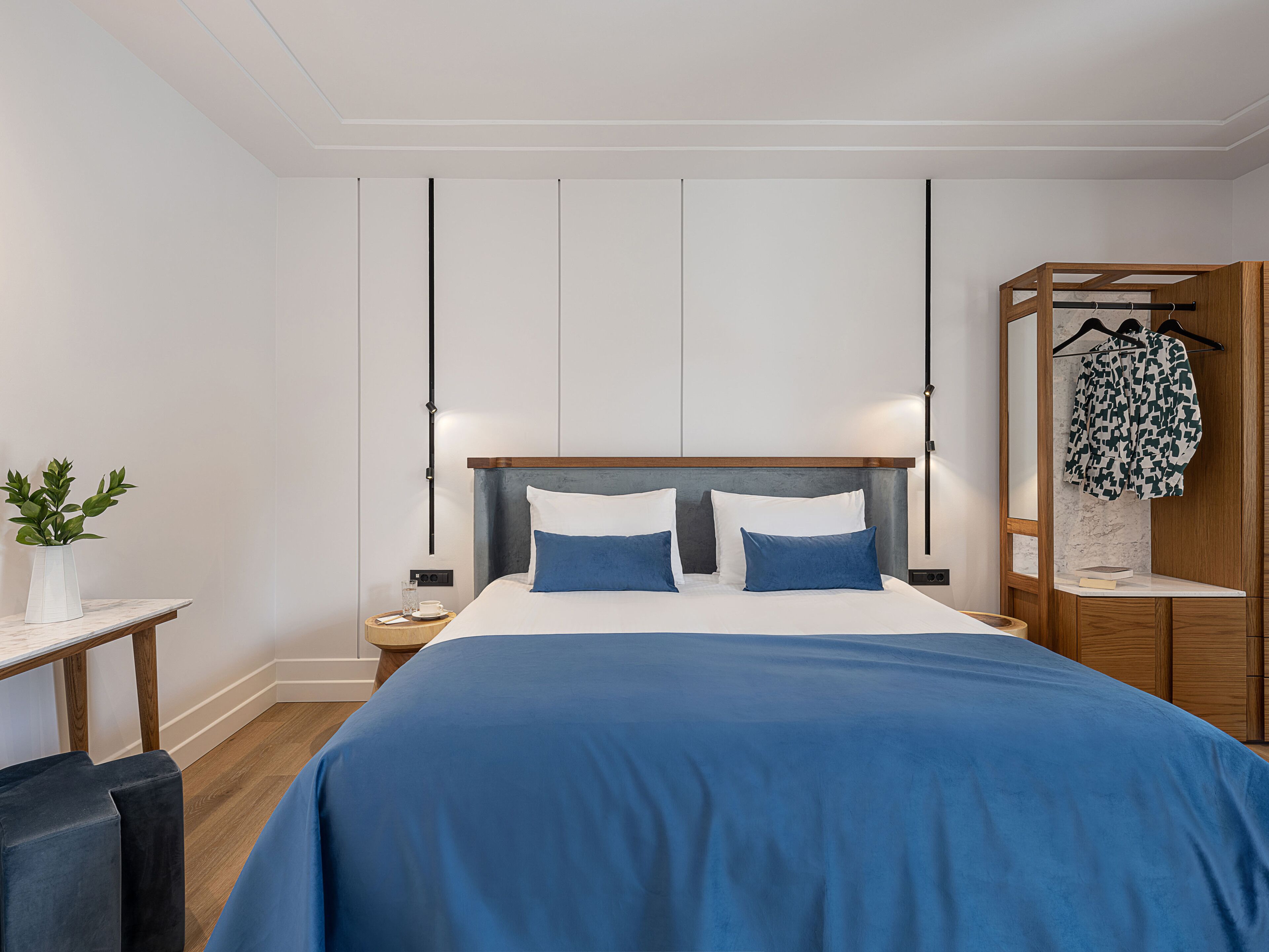 Ein modernes Hotelzimmer mit einem großen Bett, Nachttischen, einem Holzschrank und einer Topfpflanze.