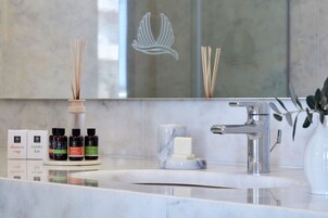 A bathroom with a marble sink, a mirror, and a vanity with toiletries.