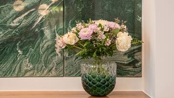 A vase with flowers on a wooden surface against a wall with a green marble-like pattern.