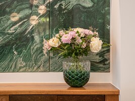 A vase with flowers on a wooden surface against a wall with a green marble-like pattern.