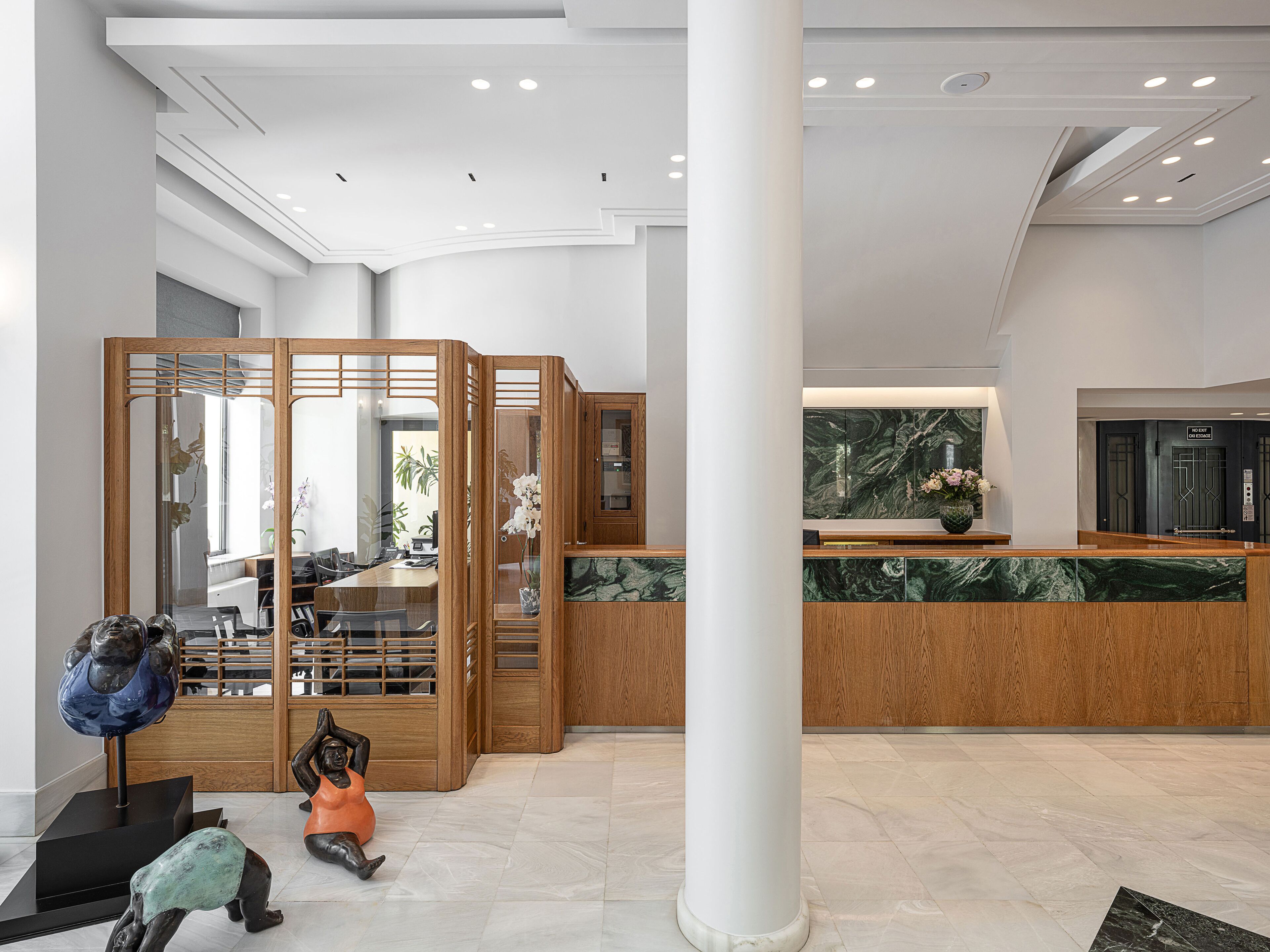 A modern hotel lobby with a reception desk, wooden partitions, and a large white column.