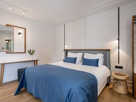 A modern bedroom with a large bed, a bedside table, a mirror, and a small stool.