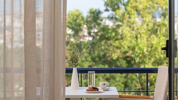 A balcony with a table set for a meal, a wicker chair, a white vase with greenery, and a clear glass bottle.